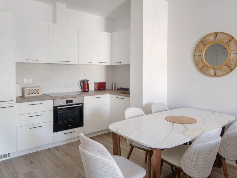 Moderne weiße Küche mit Essbereich und runder Wanddekoration in hellen Farben.