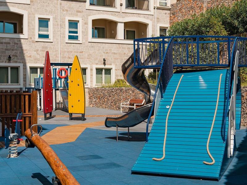 Kinderspielplatz mit Kletternetz, Rutsche und Wippe vor einem mehrstöckigen Wohngebäude.