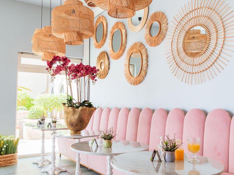 Modernes Café mit rosa Polstermöbeln, runden Marmor- und Holztischen und dekorativen Lampen und Wandspiegeln.