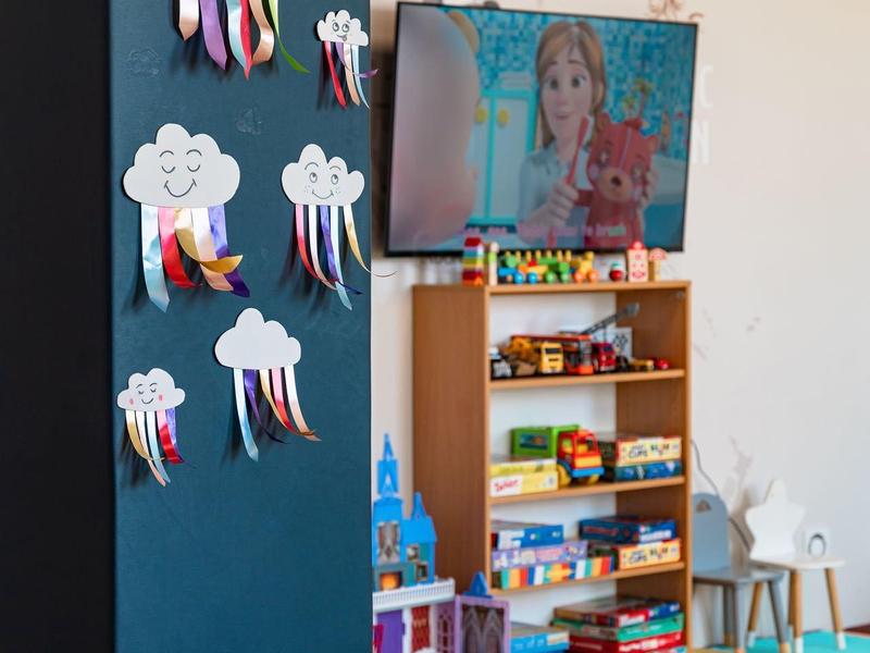 Kinder-Eckenbereich mit buntem Teppich, Spielzeugregalen und Wolken-Dekoration an der Wand.