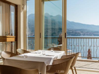 Una luminosa sala da pranzo con tavolo apparecchiato con vista su un lago e montagne attraverso grandi finestre.