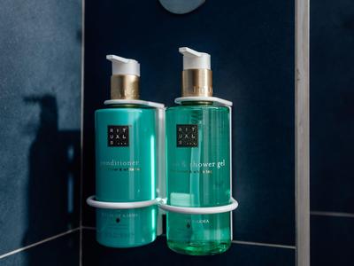 Due dispenser di sapone liquido verdi con pompe bianche accanto a un supporto bianco su una parete blu scuro.