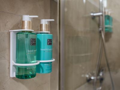 Due dispenser di sapone verdi fissati a una parete piastrellata all'interno di una doccia con parete in vetro.