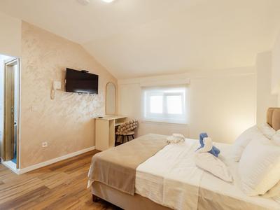 Camera d'hotel luminosa con letto matrimoniale, TV a muro e piccola scrivania sotto la finestra.