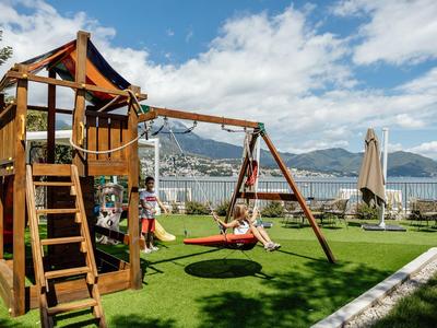 Parco giochi per bambini con altalena e scivolo su prato dell'hotel con vista montagna.