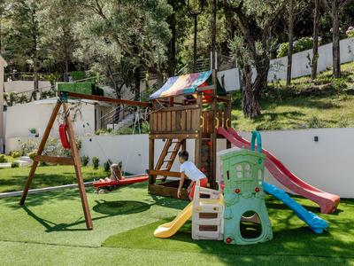 Bambino che gioca in un parco giochi colorato con scivoli e altalene su un prato erboso.