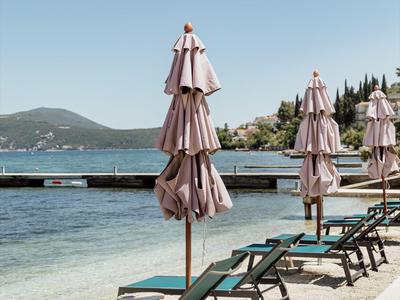 Ombrelloni chiusi e lettini su una spiaggia tranquilla con vista sul mare e sulle montagne.