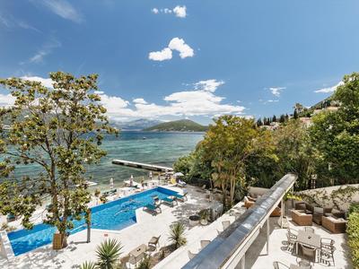 Vista di una piscina con lettini accanto a un grande specchio d'acqua e colline boscose sullo sfondo.