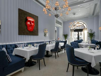 Elegantní restaurace s bílými ubrusy, modrými židlemi a moderním uměním na stěnách.