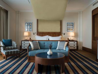 Modern eingerichtetes Schlafzimmer mit blauem Sofa, Holzkommode und gestreiften Teppichboden.