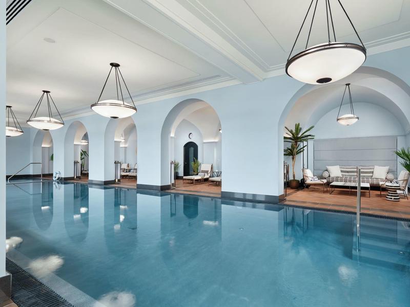 Innenpool in einem eleganten Raum mit weißblauen Wänden, Bögen und modernen Hängelampen.