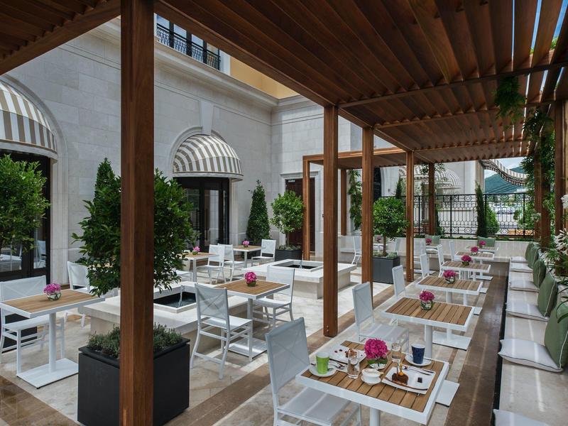 Moderner Außenbereich mit weißen Tischen, Stühlen und Holzpergola, dekoriert mit Pflanzen und Blumen.