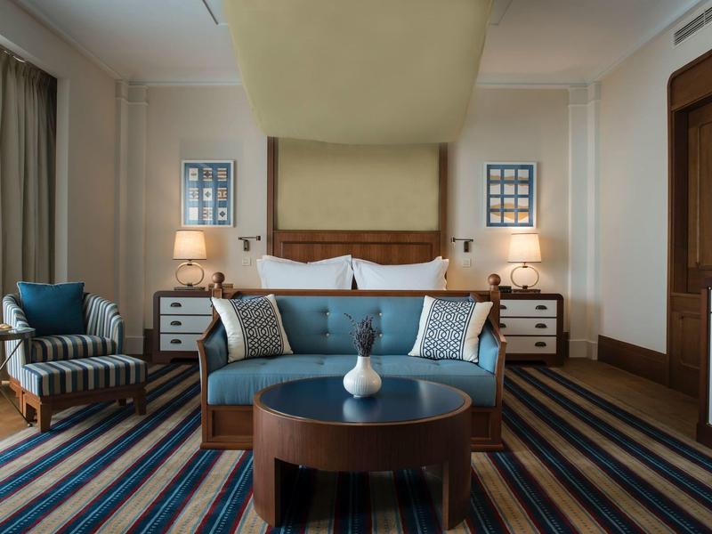 Modern eingerichtetes Schlafzimmer mit blauem Sofa, Holzkommode und gestreiften Teppichboden.