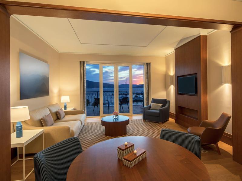 Gemütliches Wohnzimmer mit Sofa, Couchtisch und großen Fenstern zum Balkon bei Abendlicht.