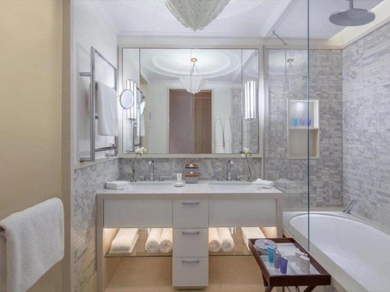 Modernes Badezimmer mit weißem Waschbecken, großer Spiegelwand, Glastrennwand und Badewanne.