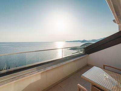 Balkon mit Glasgeländer und Tisch, Blick auf das Meer bei Sonnenuntergang.