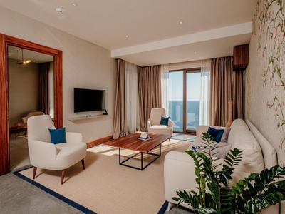 Helles Wohnzimmer mit Sofa, Sesseln, TV und großem Fenster mit Blick auf das Meer.