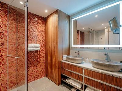 Moderne Badezimmer mit beleuchtetem Spiegel, Doppelwaschbecken und Mosaik-Duschwand.