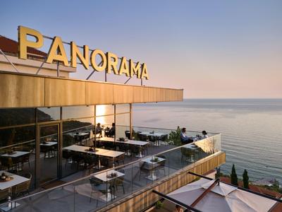 Dachterrasse eines Hotels mit Tischen und Stühlen mit Blick aufs Meer bei Sonnenuntergang.