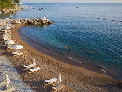 Strand mit Liegestühlen und Sonnenschirmen an ruhiger Küste mit klarem Wasser.