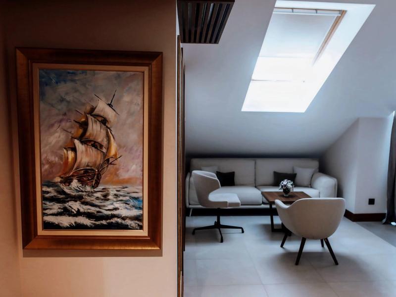 Gemälde eines Segelschiffs an einer Wand neben einem modernen Sitzbereich mit Sofa und Stühlen