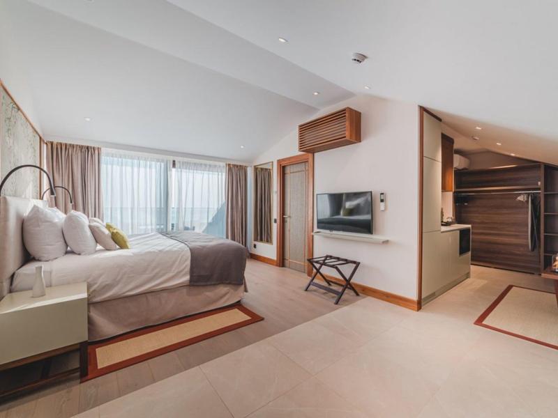 Modernes Hotelzimmer mit Doppelbett, Fernseher und einer Sitzgelegenheit unter einer Schräge.