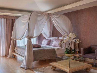 Elegantes Schlafzimmer mit Himmelbett, beigem Teppich und weichen Vorhängen.