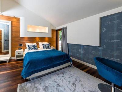 Modernes Hotelzimmer mit Doppelbett, blauem Überwurf und Sesseln, Holzfußboden und Akzentwand.