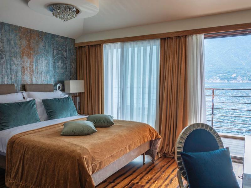 Modernes Hotelzimmer mit Doppelbett, Balkon und Blick auf einen See.