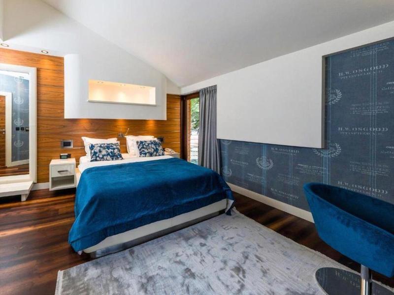 Modernes Hotelzimmer mit Doppelbett, blauem Überwurf und Sesseln, Holzfußboden und Akzentwand.