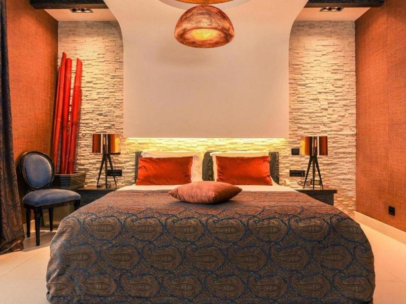 Modernes Schlafzimmer mit gemütlichem Bett, Steinwand und warmen Beleuchtungselementen.