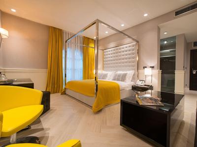 Modernes Hotelzimmer mit gelben Akzenten, einem großen Bett und stilvollen Möbeln.