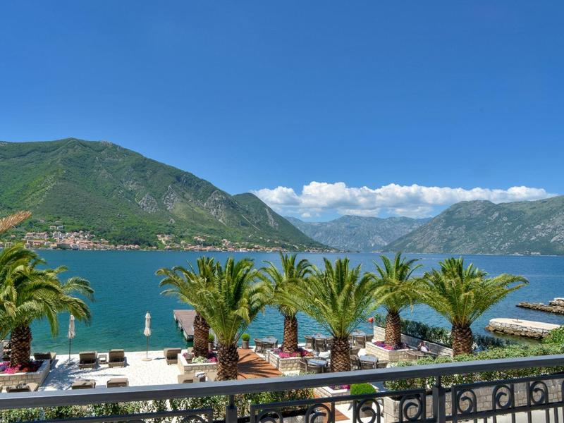 Blick auf eine Seelandschaft mit Palmen, Bergen und einem sonnigen Himmel.