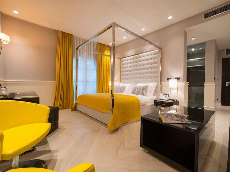Modernes Hotelzimmer mit gelben Akzenten, einem großen Bett und stilvollen Möbeln.
