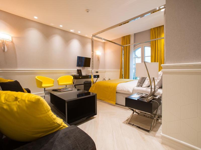 Gemütliches Hotelzimmer mit gelben Akzenten, Sofa, Bett und Schreibtisch in warmem Licht.