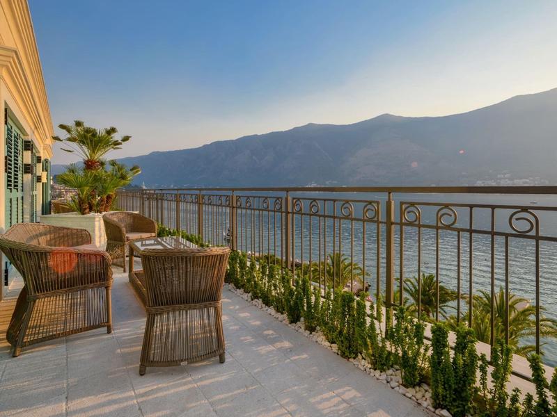 Balkon mit Stühlen und Tisch mit Blick auf See und Berge bei Sonnenuntergang.
