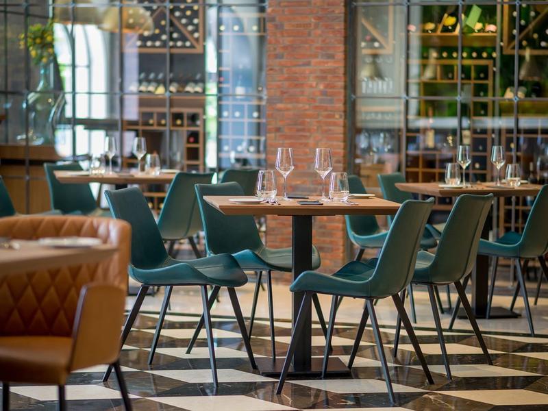 Moderner Hotelrestaurantbereich mit grünen Stühlen und Glastischen auf gemustertem Boden.