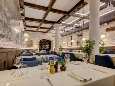 Elegantes Restaurant mit weißen Tischtüchern, blauen Stühlen und rustikalem Steinmauerambiente.