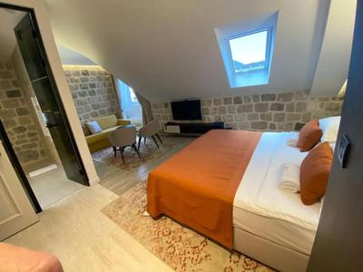 Modernes Hotelzimmer mit Dachfenster, Bett mit orangenem Überwurf und Sitzbereich mit Sofa und Fernseher.