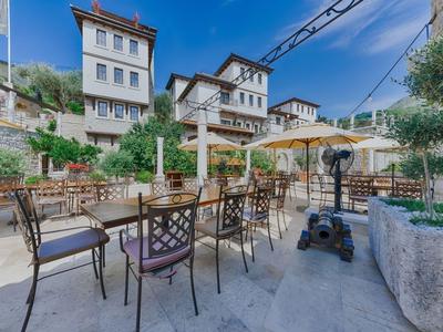 Freiluftterrasse eines Hotels mit Tischen, Stühlen und Sonnenschirmen vor traditionellen Häusern.