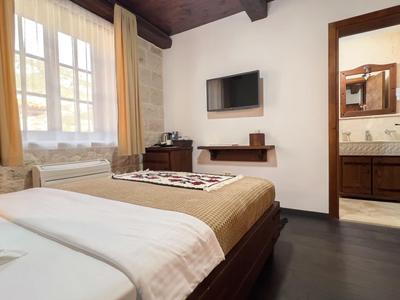 Hotelzimmer mit Doppelbett, Fenster mit Vorhängen, Fernseher an der Wand und offenem Bad