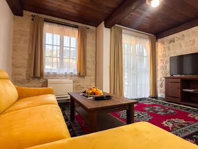 Gemütliches Wohnzimmer mit gelbem Sofa, Holztisch, Teppich und Steinwand, typisch für eine Ferienwohnung.