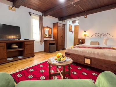 Ein gemütliches Hotelzimmer mit Doppelbett, rotem Teppich, grünem Sessel und Fernseher auf Holzmöbeln.