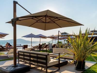 Schattiger Lounge-Bereich mit Sonnenschirmen und Liegestühlen am Strand mit Blick auf das Meer.