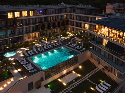 Hotel mit beleuchtetem Pool und Liegestühlen bei Nacht in moderner Architektur.