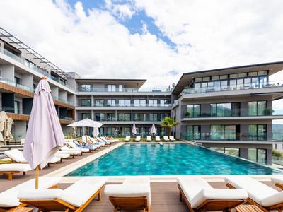 Moderner Hotelpool mit Liegestühlen und Sonnenschirmen, umgeben von mehrstöckigem Gebäude.