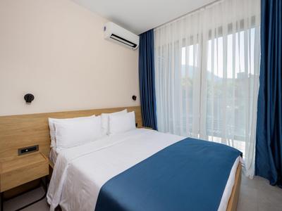 Modernes Hotelzimmer mit Doppelbett, weißen Bettwäsche und blauen Vorhängen neben großem Fenster.