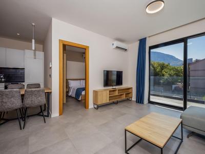 Moderner Wohnraum mit Küchenzeile, Esstisch, TV und Blick auf Balkon und Berge.