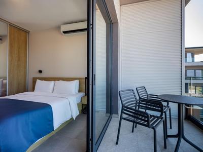 Hotelzimmer mit Bett, blauer Decke und Balkon mit Stühlen und Tisch