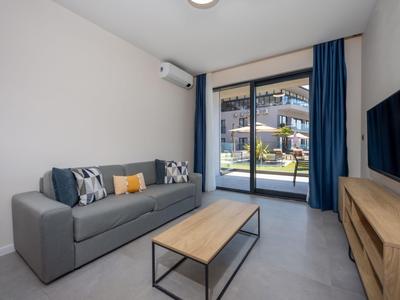 Modernes Wohnzimmer mit grauem Sofa, Holztisch und TV, mit Zugang zu einer Terrasse.